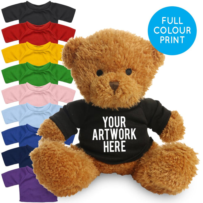 A brown plush teddy bear wearing a black custom-printed shirt with white text reading 'YOUR ARTWORK HERE,' shown on a white background with a blue circle that says 'FULL COLOUR PRINT.' A row of small teddy-bear shirts in different colors appears along the left side.